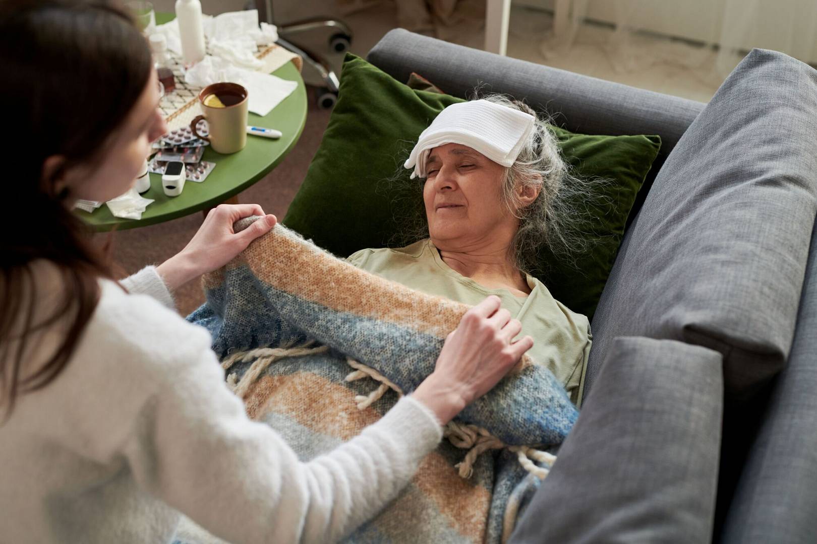 senior-woman-resting-sick-sofa-while-caregiver-covering-her.jpg
